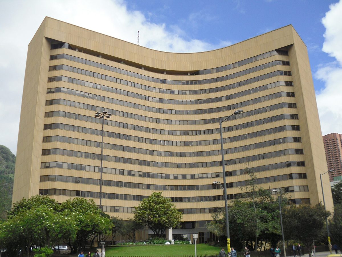 A tall, curved, sand-coloured Banco de Bogotá office tower in Bogotá, with ribbon windows, trees and a lawn in front