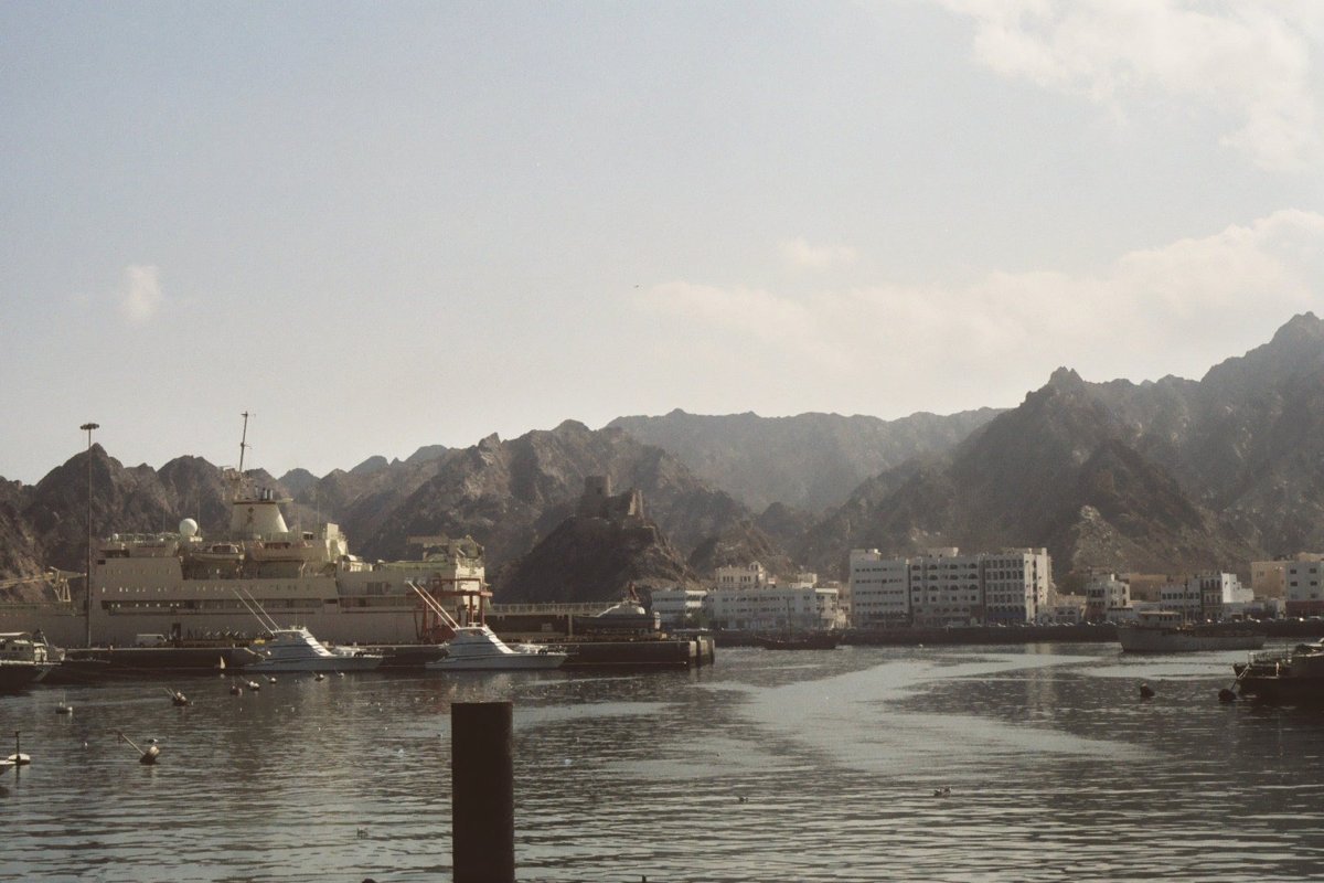 Muttrah harbour in Muscat, Oman, with waterfront buildings, moored vessels and rocky mountains