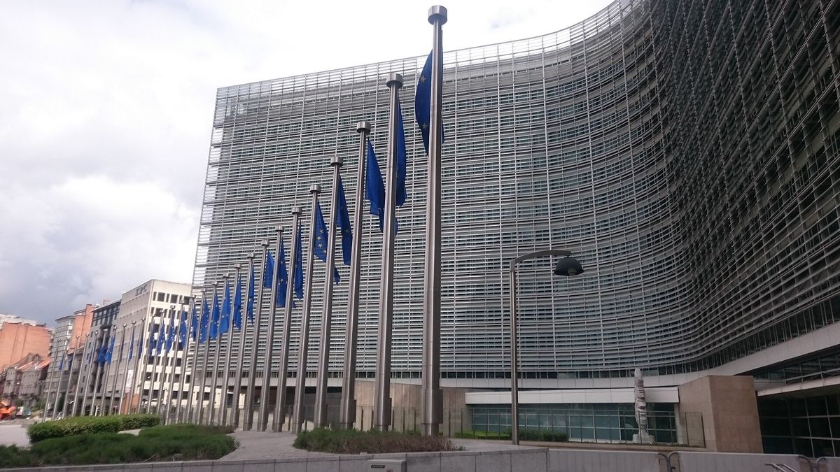 The curved glass façade of the Berlaymont building in Brussels with a row of EU flags in front