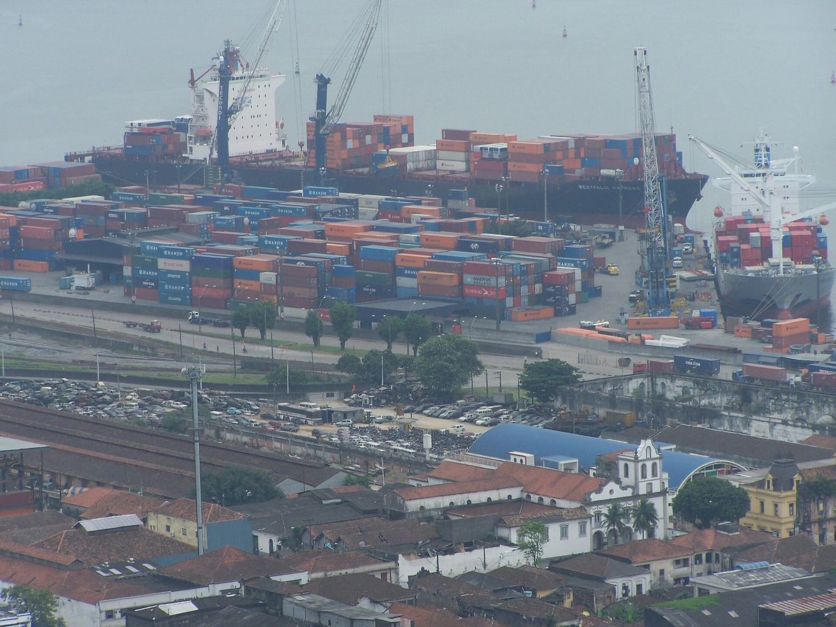 Stacked shipping containers and cargo ships at the Port of Santos beside the city’s rooftops
